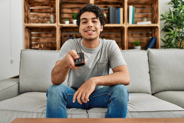 Jovem hispânico assistindo tv sentado no sofá em casa. - Foto, Imagem