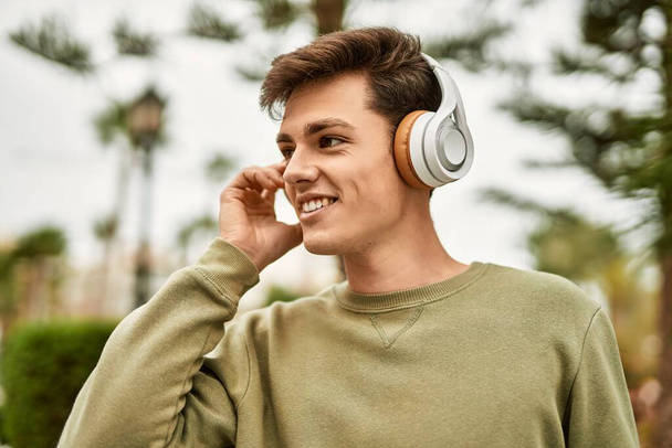 Młody Latynos uśmiecha się szczęśliwy używając słuchawek w mieście. - Zdjęcie, obraz