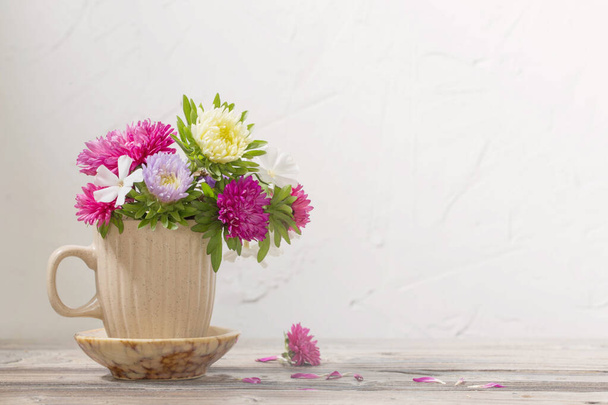 beautiful flowers in cup on wooden table on background white wall - Foto, immagini