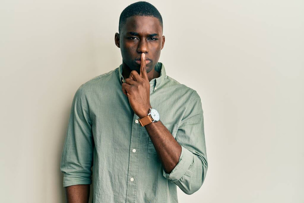 Νεαρός Αφροαμερικάνος που φοράει καθημερινά ρούχα και ζητάει ησυχία με το δάχτυλο στα χείλη. σιωπή και μυστική έννοια.  - Φωτογραφία, εικόνα
