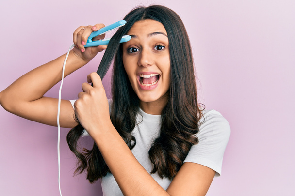 Young hispanic woman holding hair straightener celebrating crazy and amazed for success with open eyes screaming excited.  - Foto, Imagem