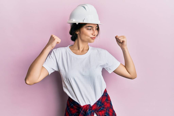 Young caucasian woman wearing hardhat showing arms muscles smiling proud. fitness concept.  - Photo, Image
