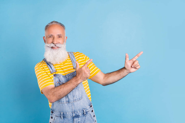 Photo of nice elder white man point empty space wear yellow t-shirt overall isolated on blue color background - Фото, зображення