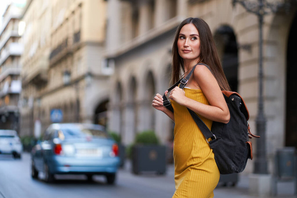 νεαρή γυναίκα διασχίζει ένα δρόμο με κίνηση με το σακίδιό της στην πλάτη της - Φωτογραφία, εικόνα