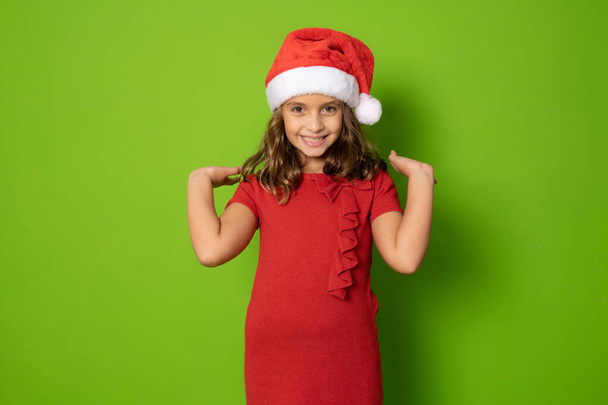 Glückliches kleines Mädchen mit Weihnachtsmütze isoliert über grünem Hintergrund. - Foto, Bild