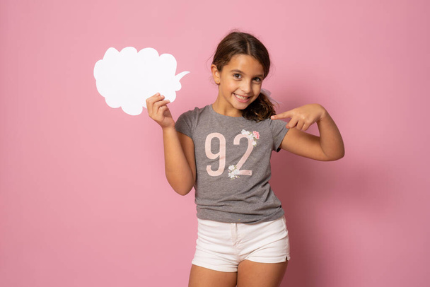 Retrato de niña alegre sosteniendo espacio de copia en la nube de papel aislado sobre fondo rosa - Foto, Imagen