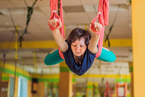 Senior mature woman practices anti-gravity yoga with a hammock in a studio. Lifestyle - 写真・画像