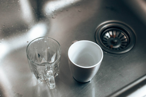 Vuil glas en keramische bekers in de wasbak, afwassen - Foto, afbeelding