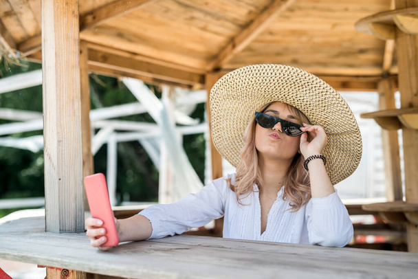 pretty lady holding cell and doing selfie near wooden gazebo at hot summer day. relax and enjot at nature - Фото, зображення