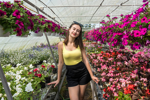 Photo of beautiful young girl posing between flowers in a greenhouse. Lifestyle - Zdjęcie, obraz