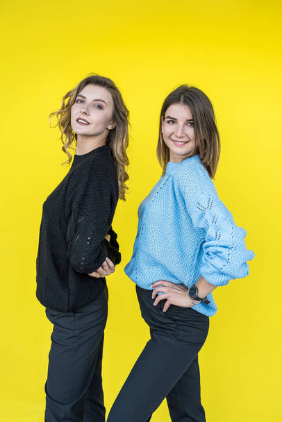 young girlfriends posing together in modern knitted sweaters isolated on yellow wall studio portrait - 写真・画像