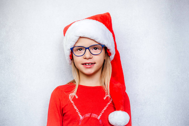 Ευτυχισμένο κοριτσάκι φορώντας γυαλιά και καπέλο Αϊ Βασίλη κατά τη διάρκεια των διακοπών των Χριστουγέννων και της Πρωτοχρονιάς - Φωτογραφία, εικόνα