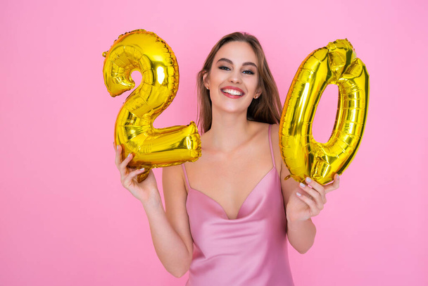 Young teenager smiling girl holds gold foil balloon on pink background. BIRTHDAY PARTY concept - 写真・画像