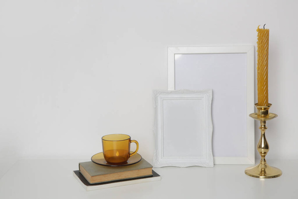 Marcos de madera blanca maqueta en la mesa con elementos de decoración interior del hogar, taza de té y candelabro. Fondo de pared blanco. - Foto, imagen