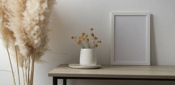 Горизонтальна біла рамка макет на столі з керамічною вазою з жовтими сухими вічними квітами. Білий фон стіни
. - Фото, зображення
