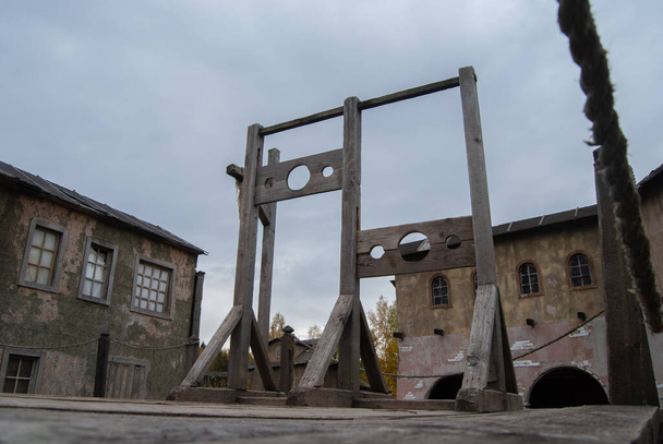 Σκιάχτρο με δύο τετράγωνα για εγκληματίες στο φόντο των σπιτιών μιας εγκαταλελειμμένης μεσαιωνικής πόλης. Μεσαιωνικό όπλο εκτέλεσης - Φωτογραφία, εικόνα