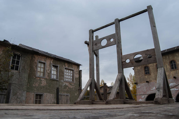 Скаффолд с двумя блоками для преступников на фоне домов заброшенного средневекового города. Средневековое оружие - Фото, изображение