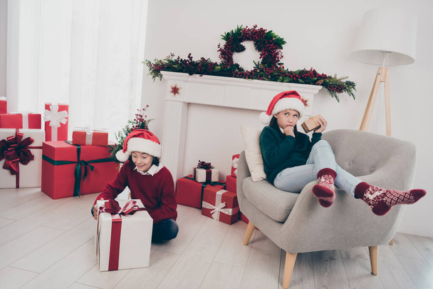 Photo of two curious funny kids prepare unpack x-mas present boxes wear jumper hat in decorated home indoors - Foto, imagen