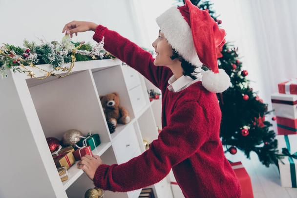 Photo of curious funny little boy investigate x-mas decorations wear jumper hat in decorated home indoors - Fotografie, Obrázek