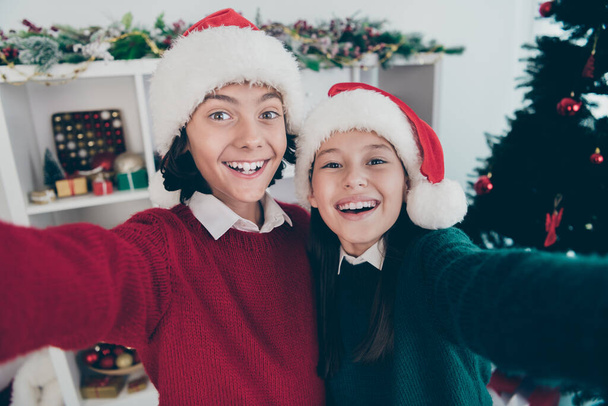 Photo of two positive kids relatives hug take selfie beaming smile wear x-mas hat jumper in decorated home indoors - Foto, imagen