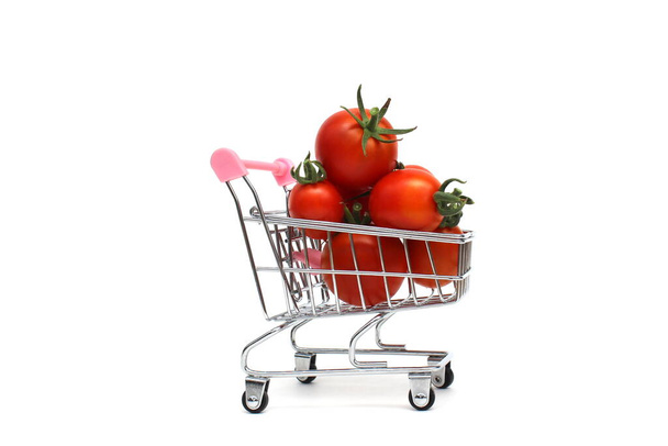 There are a bunch of ripe little tomatoes in a miniature shopping cart. - Foto, afbeelding