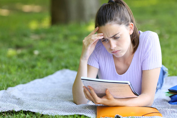 Huolestunut opiskelija opiskelee lukemista muistiinpanoja makaa kampuksella tai puistossa - Valokuva, kuva