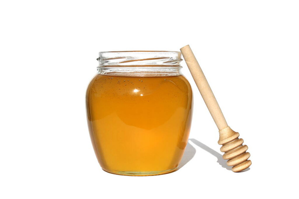 Fresh honey in a jar with a wooden dipper on a white isolated background. - Fotoğraf, Görsel