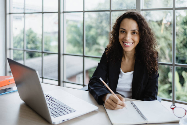 Jeune femme d'affaires écrire un cahier avec ordinateur portable sur son bureau. - Photo, image