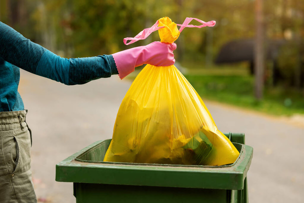 hand zet een gele plastic ongesorteerde vuilniszak in de prullenbak. huishoudelijk afval - Foto, afbeelding
