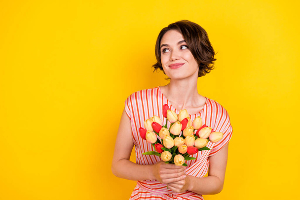 Portrait of attractive dreamy cheerful girl holding tulips thinking copy space isolated over bright yellow color background - Photo, image
