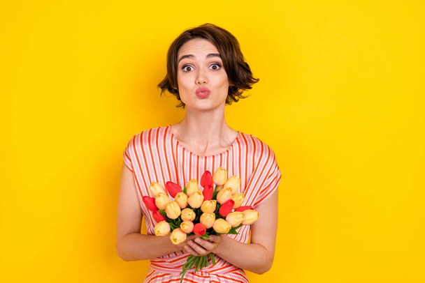 Retrato de chica coqueta atractiva sosteniendo tulipanes enviando beso de aire amour aislado sobre fondo de color amarillo brillante - Foto, imagen