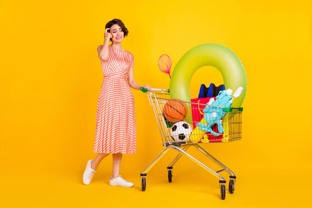 Photo of doubtful troubled girl carry shop cart think wear striped dress shoes isolated yellow color background - Valokuva, kuva