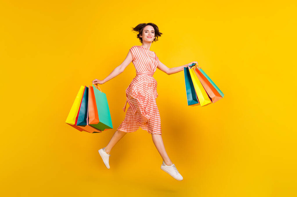 Full length body size view of lovely girl carrying bags bargain jumping going isolated over bright yellow color background - Valokuva, kuva