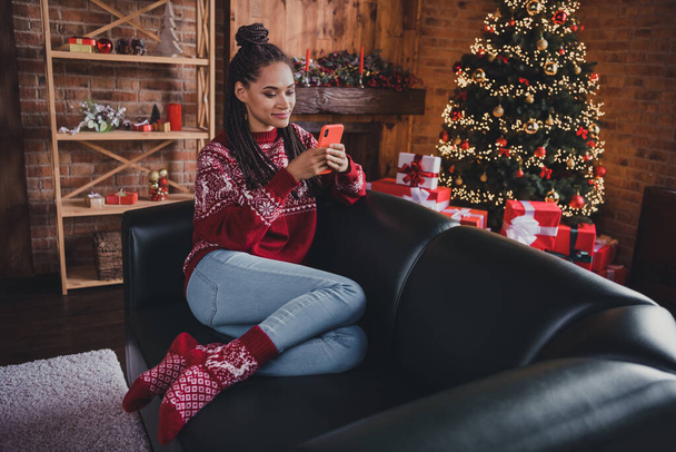Photo of cheerful lady sit couch hold telephone read congrats sms wear pullover in decorated home indoors - Φωτογραφία, εικόνα