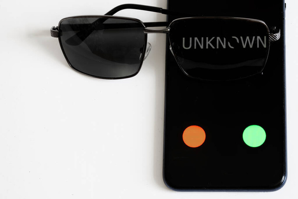 Das Smartphone mit einem unbekannten Anruf liegt auf einem weißen Tisch neben einer Sonnenbrille. Das Problem der Sicherheit persönlicher Daten, Anonymität und Spionage mit modernen Geräten. Schutz persönlicher Daten - Foto, Bild