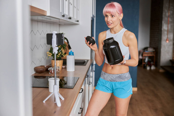 Захоплена жінка показує велику банку дієтичної додаткової стрільби на камеру на кухні
 - Фото, зображення