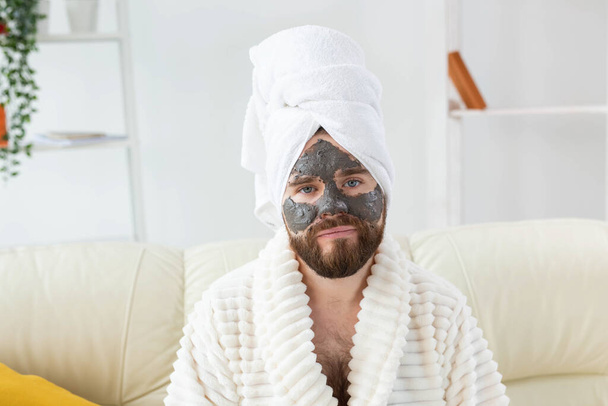 Brodaty mężczyzna ma czystą, świeżą skórę, nosi na twarzy glinianą maskę i lubi zabiegi kosmetyczne. Spa w domu, pielęgnacja ciała i skóry - Zdjęcie, obraz