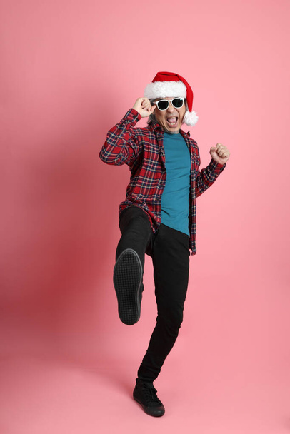 Ο ηλικιωμένος Ασιάτης με το χριστουγεννιάτικο καπέλο στέκεται στο ροζ φόντο. - Φωτογραφία, εικόνα
