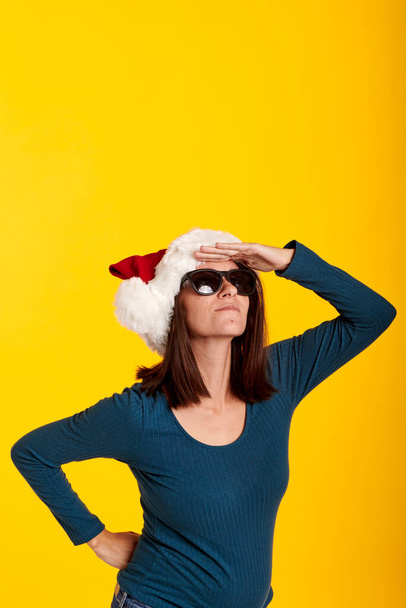 una joven con un sombrero de Santa Claus con un fondo amarillo - Foto, Imagen
