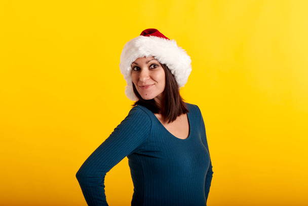 una joven con un sombrero de Santa Claus con un fondo amarillo - Foto, imagen