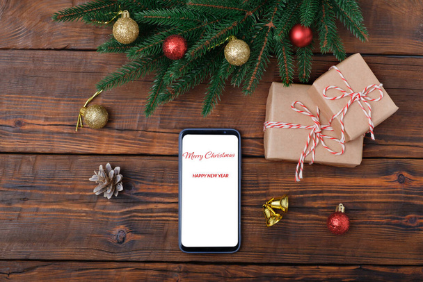 Μοντέρνο smartphone με mockup σε ξύλινο vintage τραπέζι με χριστουγεννιάτικη διακόσμηση, κουτί δώρου. Επίπεδο πρότυπο lay. Στεφάνι ελάτης - Φωτογραφία, εικόνα