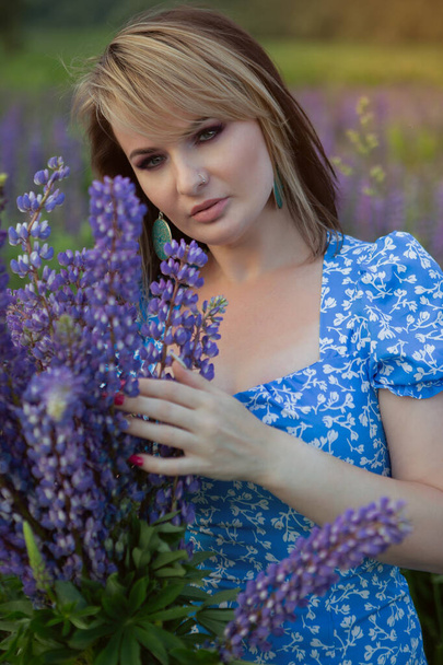 Een prachtige vrouw in een lange lichte zomer jurk en hoed op een veld van bloemen - Foto, afbeelding