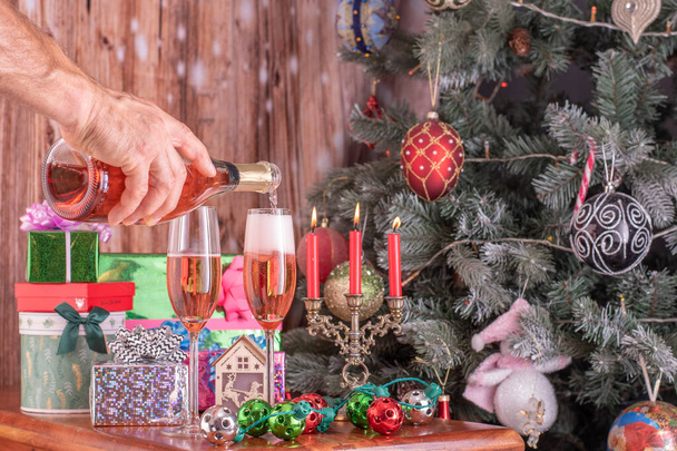 Мужчины выливают шампанское из бутылки в шампанское на фоне новогодней елки и представляют. - Фото, изображение