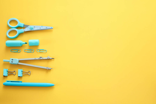 Blue stationery items on the yellow background with free space for text. Creative, colorful background with school supplies. Flatlay with copy space, top view. Marker, pen, paper clips, scissors. - Photo, Image