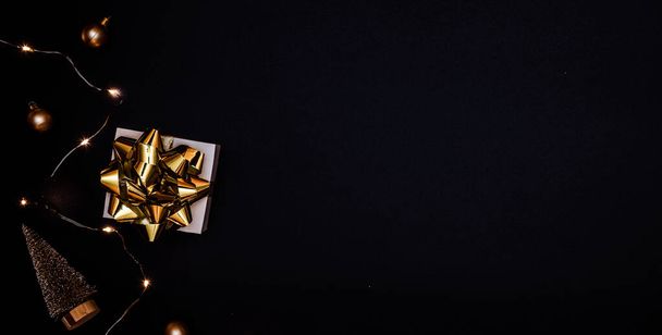 Cadeau de Noël. Cadeau blanc avec arc doré, boules d'or et guirlande de lumières scintillantes dans la décoration de Noël sur fond sombre pour carte de vœux. Fond de Noël avec espace pour le texte - Photo, image