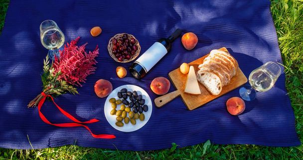 Ambiente de picnic al aire libre con hermoso ramo de astilbe rosa, copas y botella de vino blanco, pan, queso y frutas. Vista superior. - Foto, Imagen