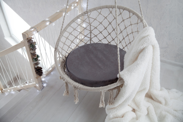 Noel 'i bekliyorum. Çelenklerle süslenmiş bir odanın arka planında beyaz kürklü bir ekoseyle sallanan sandalye. - Fotoğraf, Görsel