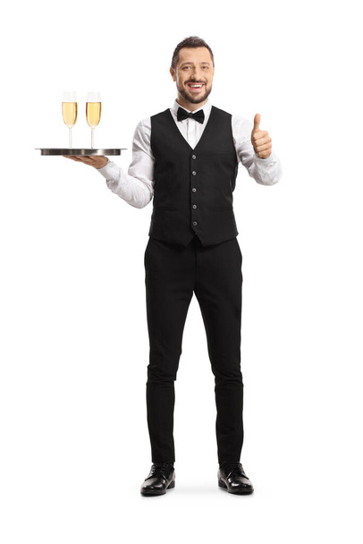 Full length portrait of a cheerful server holding a tray with glasses of white wine and showing thumbs up isolated on white background - Foto, immagini
