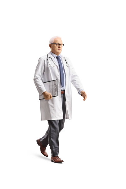 Teljes hossz lövés egy érett férfi orvos séta és a kezében egy írótábla elszigetelt fehér háttér  - Fotó, kép