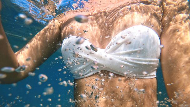 Nainen valkoisessa uimapuvussa Välimeren sinisessä ja läpinäkyvässä vedessä. Kameraa pidellen - Valokuva, kuva